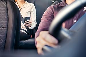 A person using a cellphone while seated in the back seat of an Uber/Lyft car